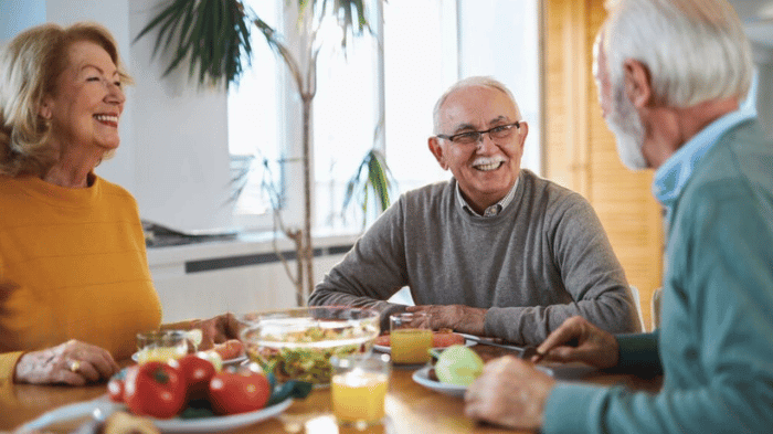 Groupe de seniors souriants partageant un repas équilibré autour d’une table, symbole de convivialité et de nutrition saine.