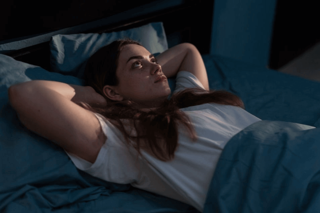 Femme allongée dans son lit, les yeux ouverts et l’air préoccupé, illustrant les troubles du sommeil fréquents pendant la ménopause.