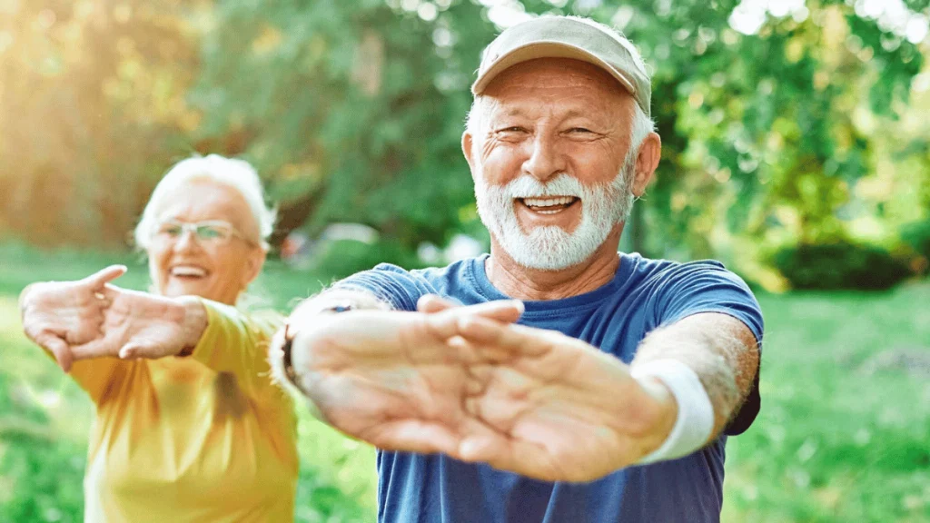 Couple senior souriant faisant des étirements ensemble en plein air, sous un beau soleil, dans un parc verdoyant.