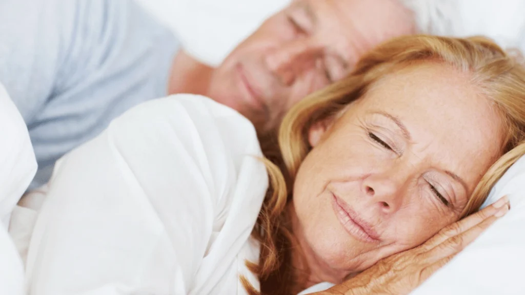 Couple senior dormant paisiblement ensemble dans un lit, blottis sous une couette blanche.